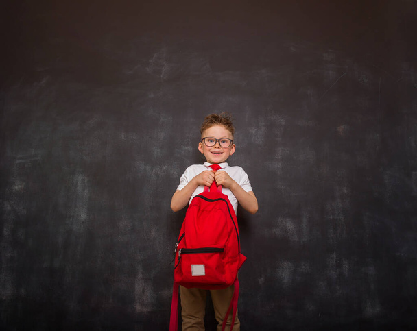 Little boy carrying heavy backpack or school bag full causing stress and pain on back due to overweight against blackboard. Back to school. - Fotoğraf, Görsel