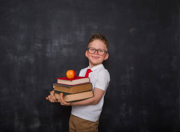 Liebenswertes Kind mit Büchern und Apfel in der Hand. Zurück zur Schule. Bildung. Tafel im Hintergrund. Junge Schüler in Uniform. - Foto, Bild