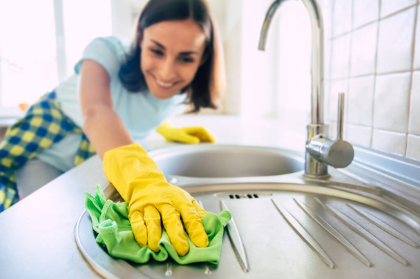 Young happy cute woman in yellow gloves is cleaning her kitchen at home - Foto, immagini