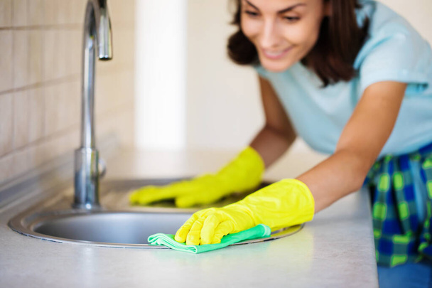 Young happy cute woman in yellow gloves is cleaning her kitchen at home - Zdjęcie, obraz