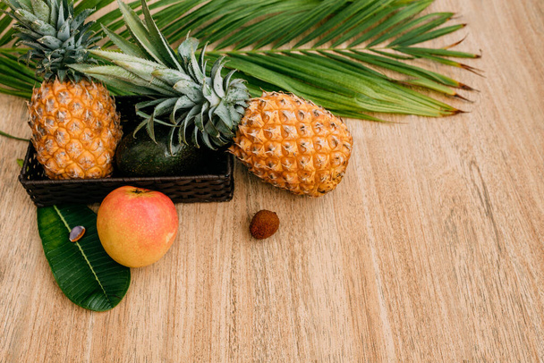 Τροπικά φρούτα σε καφέ φόντο με όμορφο φύλλο φοίνικα. Ανανάδες, μάνγκο, αβοκάντο, λίτσι. Εξωτικά φρούτα για υγιεινή διατροφή. Αντιγραφή χώρου, χώρου για κείμενο ή λογότυπο - Φωτογραφία, εικόνα
