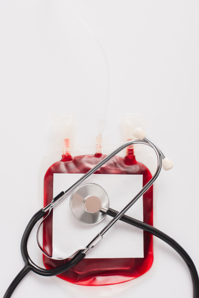 Ansicht der Blutspendeverpackung mit Blanko-Etikett und Stethoskop isoliert auf weiß - Foto, Bild