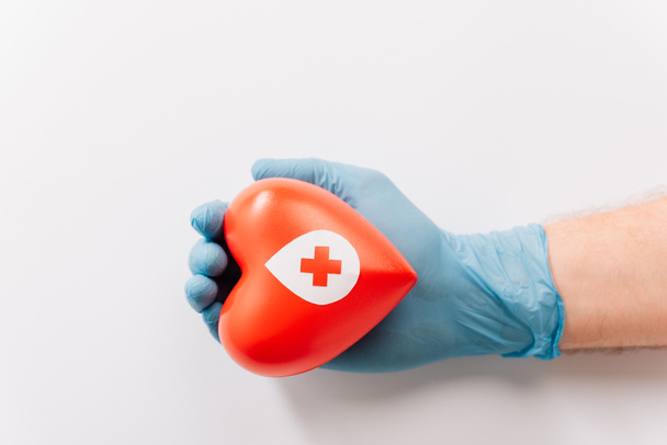 περικοπή άποψη του ανδρικού χεριού στο γάντι λατέξ με κόκκινη καρδιά σε λευκό, ιδέα αιμοδοσίας - Φωτογραφία, εικόνα
