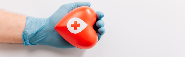 Ausgeschnittene Ansicht der männlichen Hand in Latex-Handschuh mit rotem Herz auf weißem, Blutspendekonzept - Foto, Bild