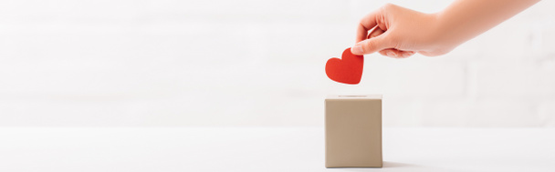cropped view of female hand putting red heart in box on white background, donation concept - Photo, Image