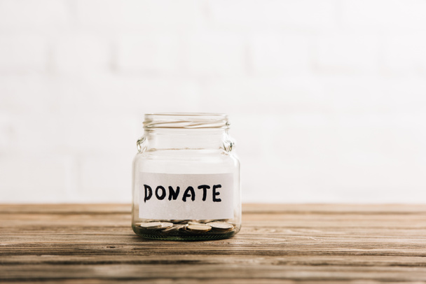 penny jar with donate lettering on wooden surface on white background - Foto, afbeelding