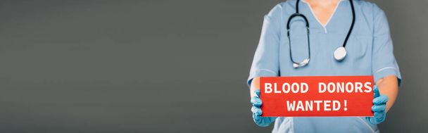 vista recortada del médico con estereoscopio con tarjeta roja con donantes de sangre quería letras aisladas en gris, tiro panorámico - Foto, Imagen