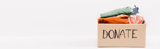 panoramatický záběr lepenkové krabice s darovaným oblečením a obuví izolovanou na bílém, charitativní koncept - Fotografie, Obrázek