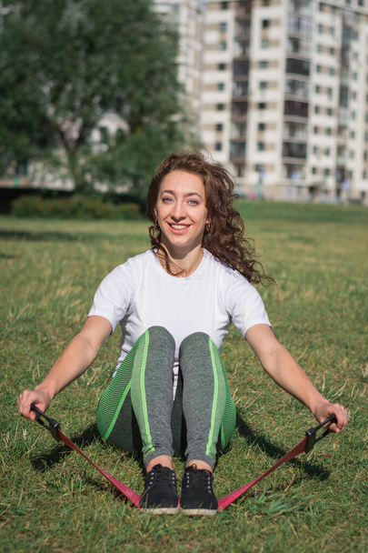 woman coach in gym leggings does sports exercise on a summer day in a park on a green lawn - Foto, afbeelding