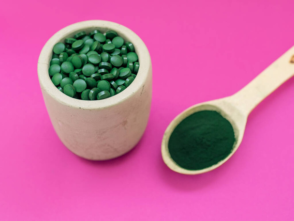 Green hawaiian spirulina in tablespoons pills and powder on pink  background. Super food, healthy lifestyle, healthy supplements concept - Foto, afbeelding