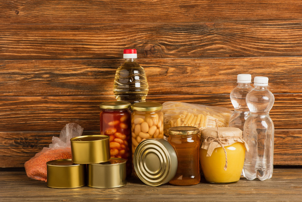 крупы возле воды, масла, консервов и меда на деревянном фоне, благотворительная концепция - Фото, изображение