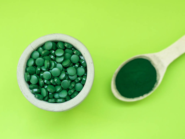 Spiruline hawaïenne verte dans des cuillères à soupe de pilules et de poudre sur fond vert clair. Super nourriture, mode de vie sain, concept de suppléments sains - Photo, image