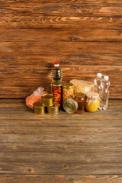 groats cerca del agua, aceite, alimentos enlatados y miel sobre fondo de madera, concepto de caridad - Foto, Imagen