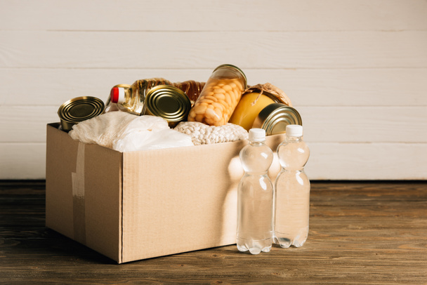 caja de cartón con alimentos donados y agua sobre fondo de madera, concepto de caridad - Foto, Imagen