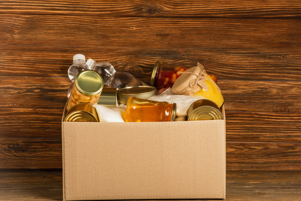 картонная коробка с пожертвованной пищей на деревянном фоне, концепция благотворительности - Фото, изображение