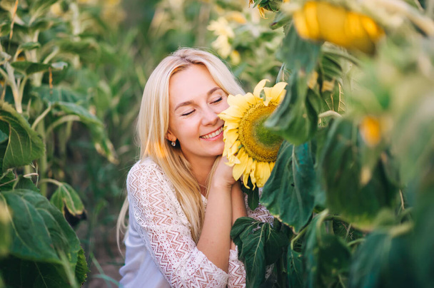 Gelukkige blonde vrouw zit in zonnebloemen. Horizontaal portret - Foto, afbeelding