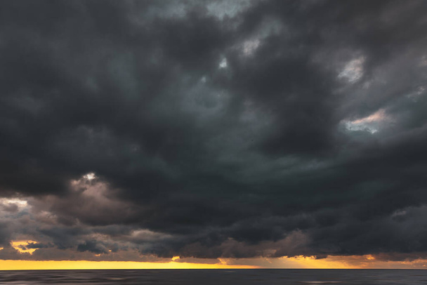 Дивовижний драматичний пейзаж. Драматичні темні хмари під час заходу сонця в морі. Темна морська вода і важкі красиві сірі хмари
. - Фото, зображення