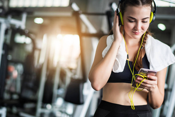 Young attractive Caucasian woman listening to music by earphones connect to smart phone or cellphone. Relaxation after hard workout in gym  - Foto, immagini