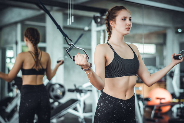 Cinematic ton młody atrakcyjny fitness kobieta ćwiczenia z maszyny w siłowni. Zdrowe, trening i dieta koncepcja stylu życia.  - Zdjęcie, obraz