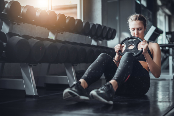 Кинематографический тон молодой привлекательной фитнес-женщины упражнения с гантели в тренажерном зале. Индивидуальный спорт, чтобы приспособить мышцы тела для здорового образа жизни.  - Фото, изображение