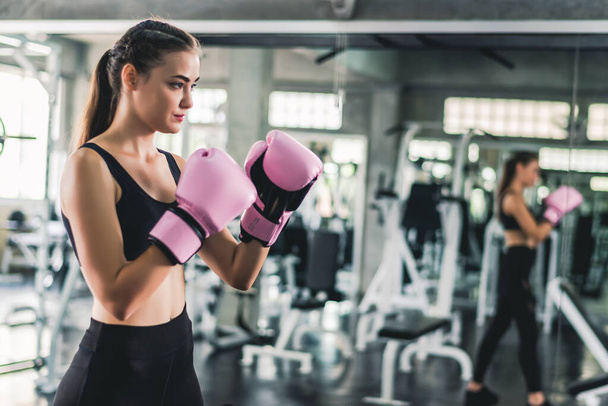 Jolie jolie femme caucasienne en gants de boxe rose sac de boxe pendant l'entraînement dans la salle de gym.  - Photo, image