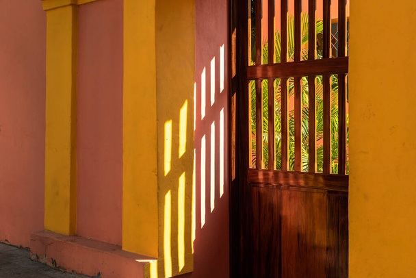 Licht und Schatten abstrakt mit Sonnenlicht, das auf die bunten Wände vor einer Holztür in der Altstadt von Pondicherry trifft. - Foto, Bild