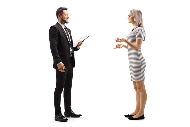 Full length profile shot of a young woman talking to a man in black suit with cliboard in his hands isolated on white background - Fotografie, Obrázek