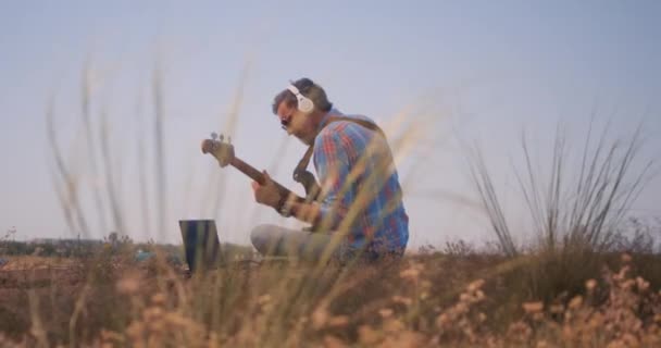 Μουσικός παίζει μπάσο κιθάρα στο ύπαιθρο - Πλάνα, βίντεο