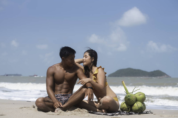 Красивый мужчина и красивая женщина в купальнике, сидя на пляже, с романтическим чувством, позируя модель - Фото, изображение