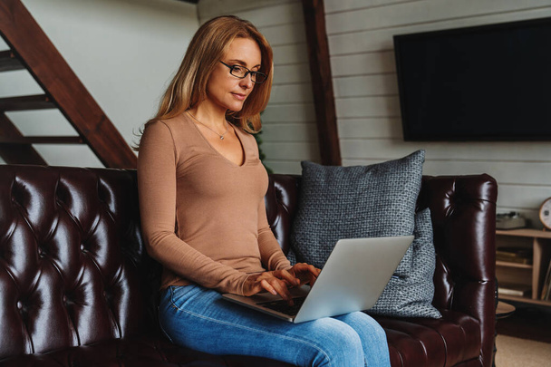 Adulto mulher branca usando computador portátil em casa na sala de estar
 - Foto, Imagem