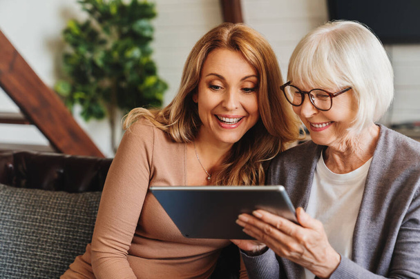 Positive senior woman and her daughter using tablet at home - Fotoğraf, Görsel
