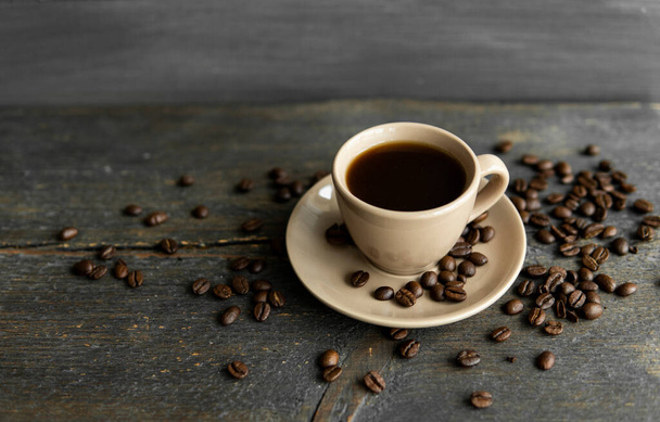 Coffee cup with roasted coffee beans on wooden table background. Mug of black coffe with scattered coffee beans on a wooden table. Fresh coffee beans. - 写真・画像