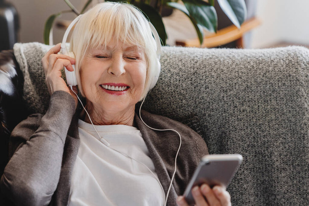 Happy mature old woman wear headphone holding smart phone relax with eyes closed - Fotografie, Obrázek