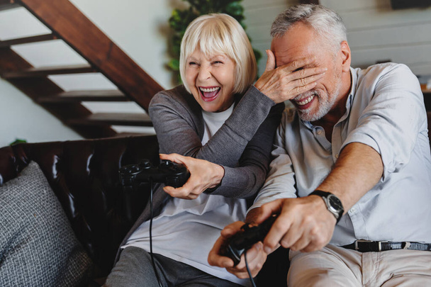 Couple of caucasian retired seniors playing video games together at home - 写真・画像