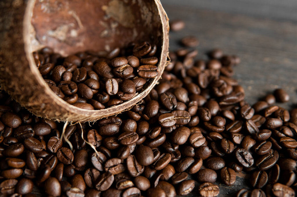 Roasted arabica coffee beans scattered on a wooden table from a coconut. Fresh coffee beans. - Photo, Image