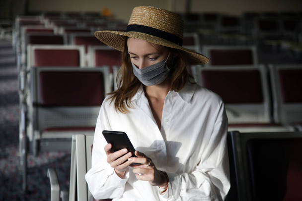Turistka s maskou a telefonem na letišti. Bezpečnostní opatření během koronaviru. Nový normální koncept.  - Fotografie, Obrázek