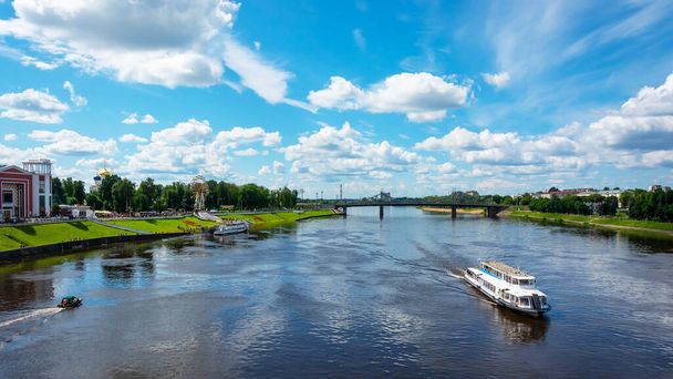 Tver / Ρωσία - 19 Ιουλίου 2020: Σκάφος αναψυχής με τουριστικά πανιά κατά μήκος του ποταμού Βόλγα. Στο βάθος είναι μια μεγάλη γέφυρα. Αριστερά είναι το πάρκο της πόλης. - Φωτογραφία, εικόνα