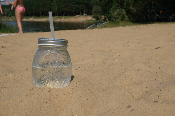 A glass of water stands on a sandy beach. - Photo, image