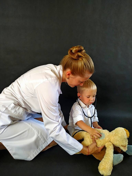female pediatrician playing with boy listening teddy bear by stethoscope - Photo, Image