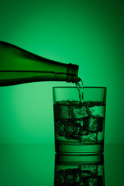 όμορφο μπουκάλι με νερό και γυαλί με πάγο και νερό σε πράσινο φόντο από κοντά - Φωτογραφία, εικόνα