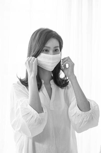 Jonge aziatische vrouw draagt chirurgische masker thuis in zwart-wit - Foto, afbeelding
