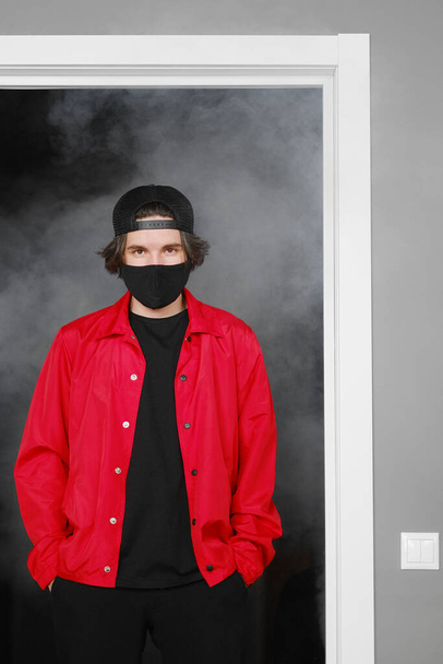 Portrait of a young man of 25-30 years old in a black protective mask, cap and red jacket.  - 写真・画像