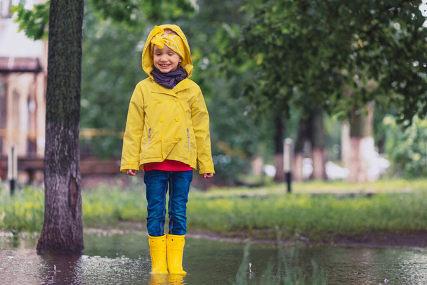 Seid nicht traurig. Mädchen in gelbem Regenmantel und Gummistiefeln in Pfützen auf einem Parkplatz, Herbstspaziergang. Glückskonzept für Kinder - Foto, Bild