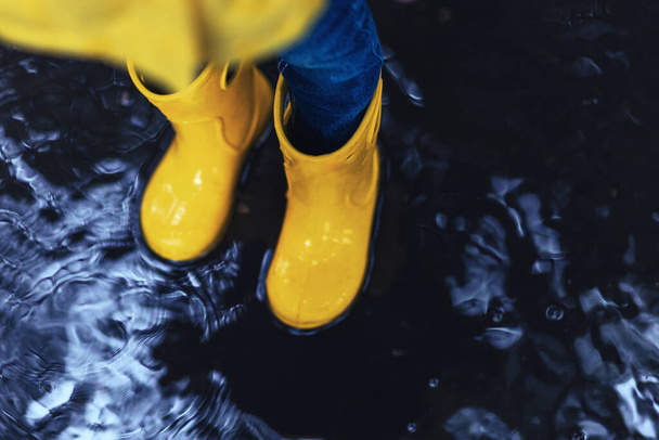 Piedi in stivali di gomma gialla in piedi in una pozzanghera, spazio copia - Foto, immagini