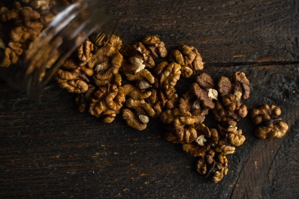 Walnut scattered on the wooden vintage table from a jar. Walnut is a healthy vegetarian protein nutritious food. Walnut kernels and whole walnuts on rustic old wood. - Photo, image