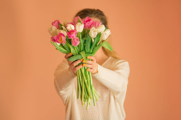 Mladý okouzlující úsměv dívka drží velkou kytici tulipánů na světle béžové pozadí. Mladá krásná dívka v bílých šatech s barevnými čerstvými květy tulipán - Fotografie, Obrázek