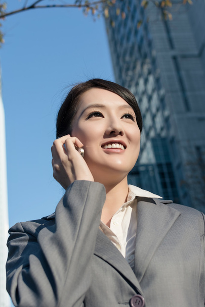 Счастливая азиатская бизнес-леди разговаривает по телефону и ходит на стуле
 - Фото, изображение