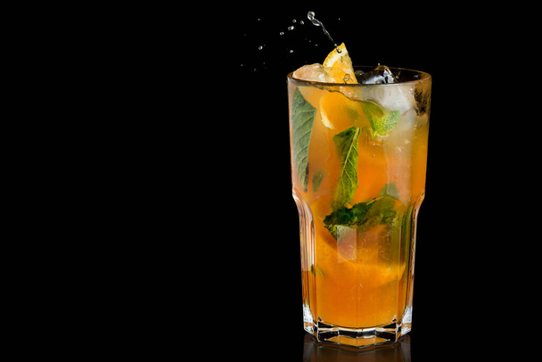 Limonada naranja fresca con hojas de menta. Salpicadura de bebida sobre fondo negro. - Foto, imagen