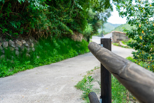 Вид на красивую проселочную дорогу с каменной стеной, деревянными перилами и большим количеством зелени. Концепция спокойствия - Фото, изображение