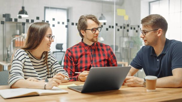Young Woman and Two Male Colleagues Having a Friendly Meeting and Discussing New Business Ideas. Easygoing Coworking Atmosphere in Loft Office Creative Agency. They Make Notes in Laptop and Tablet. - Photo, Image